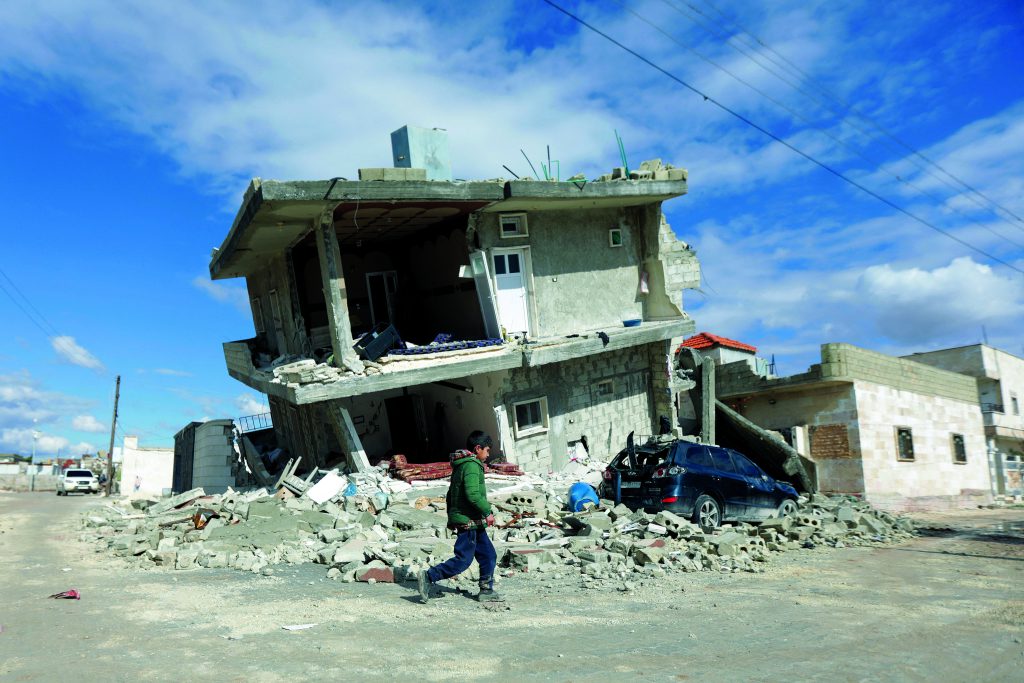 Een jongen loopt langs een ingestort huis ten gevolge van de zware aardbevingen in Syrie en Turkije in februari 2023.